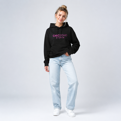 A woman modeling a black pullover hoodie with “CHICSOHO BY CHTQ” printed in pink across the chest, paired with black pants and white sneakers, against a light gray studio background.