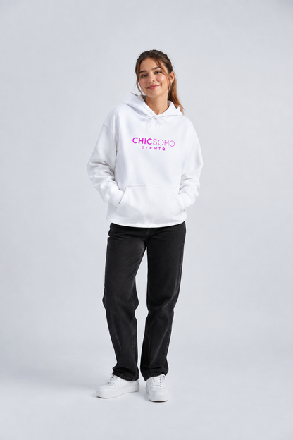 A woman modeling a white pullover hoodie with “CHICSOHO BY CHTQ” printed in pink across the chest, paired with black pants and white sneakers, against a light gray studio background.