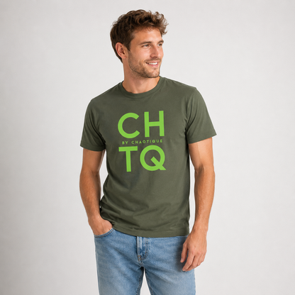 A man wearing a green graphic T-shirt with “CHTQ BY CHAOTIQUE” printed on the chest, paired with blue jeans and white sneakers, standing against a light gray studio background.