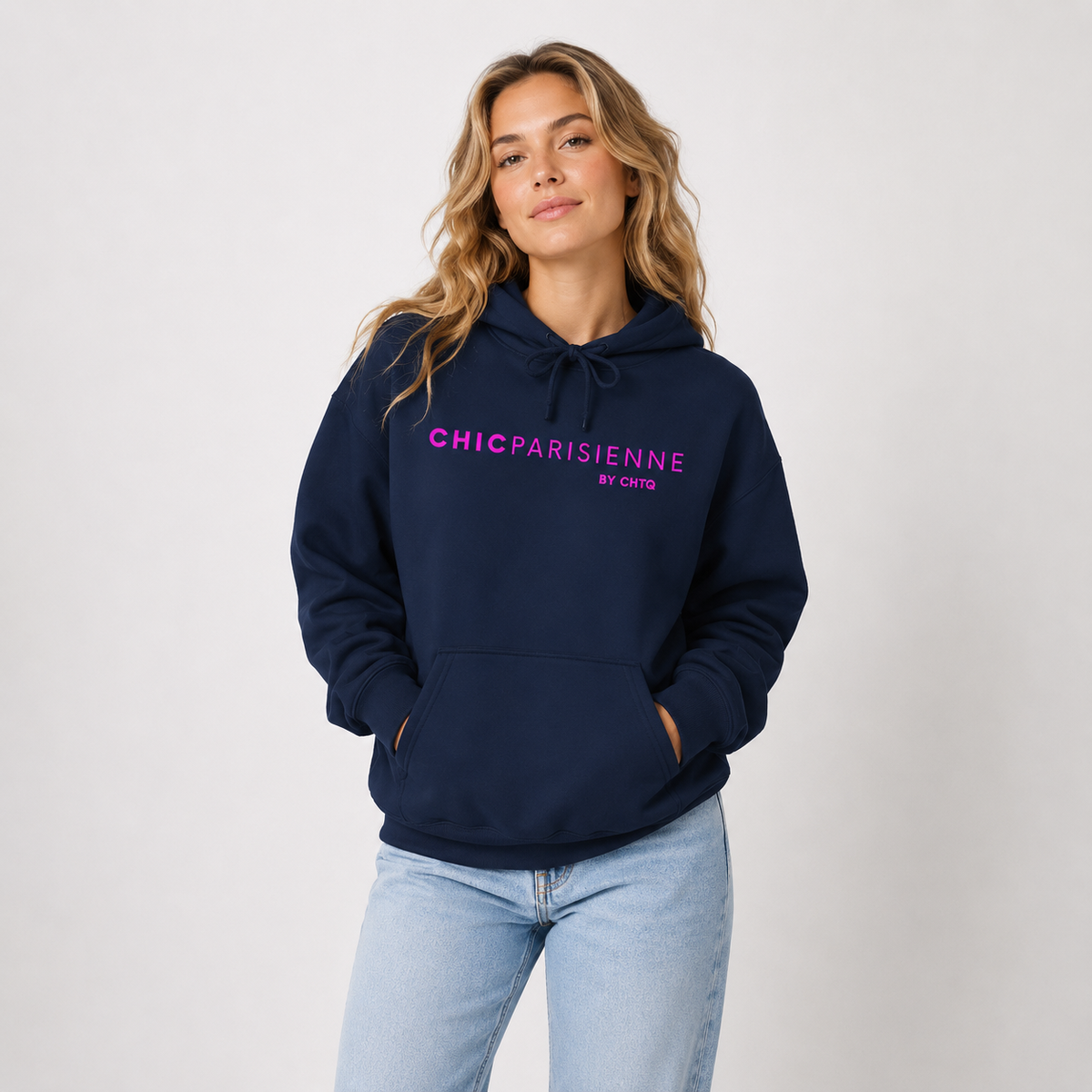 Woman wearing a navy blue CHIC PARISIENNE BY CHTQ graphic hoodie with bright pink lettering, paired with light-wash jeans in a light studio setting.