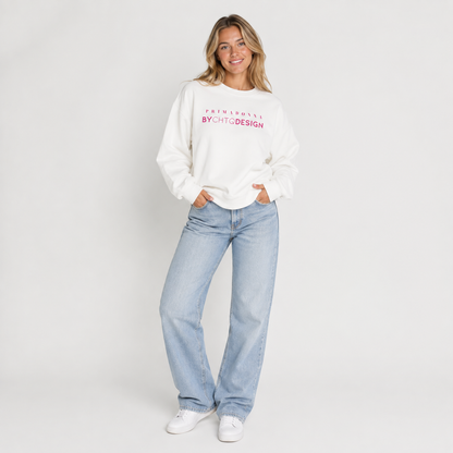 A woman wearing a white crewneck sweatshirt featuring pink “PRIMADONNA BY CHTQ DESIGN” text across the chest, paired with jeans, photographed against a light gray studio background.