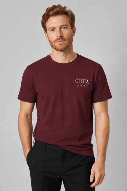 A man wearing a maroon short-sleeve t-shirt with a white 'CHTQ RAFFINE' logo on the left chest, paired with black trousers, against a solid gray studio background.