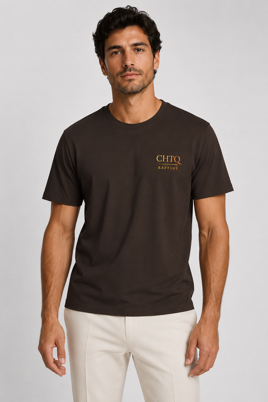 A man wearing a dark brown short-sleeve crewneck t-shirt with a gold 'CHTQ RAFFINE' logo on the left chest, paired with off-white trousers, against a light gray studio background.