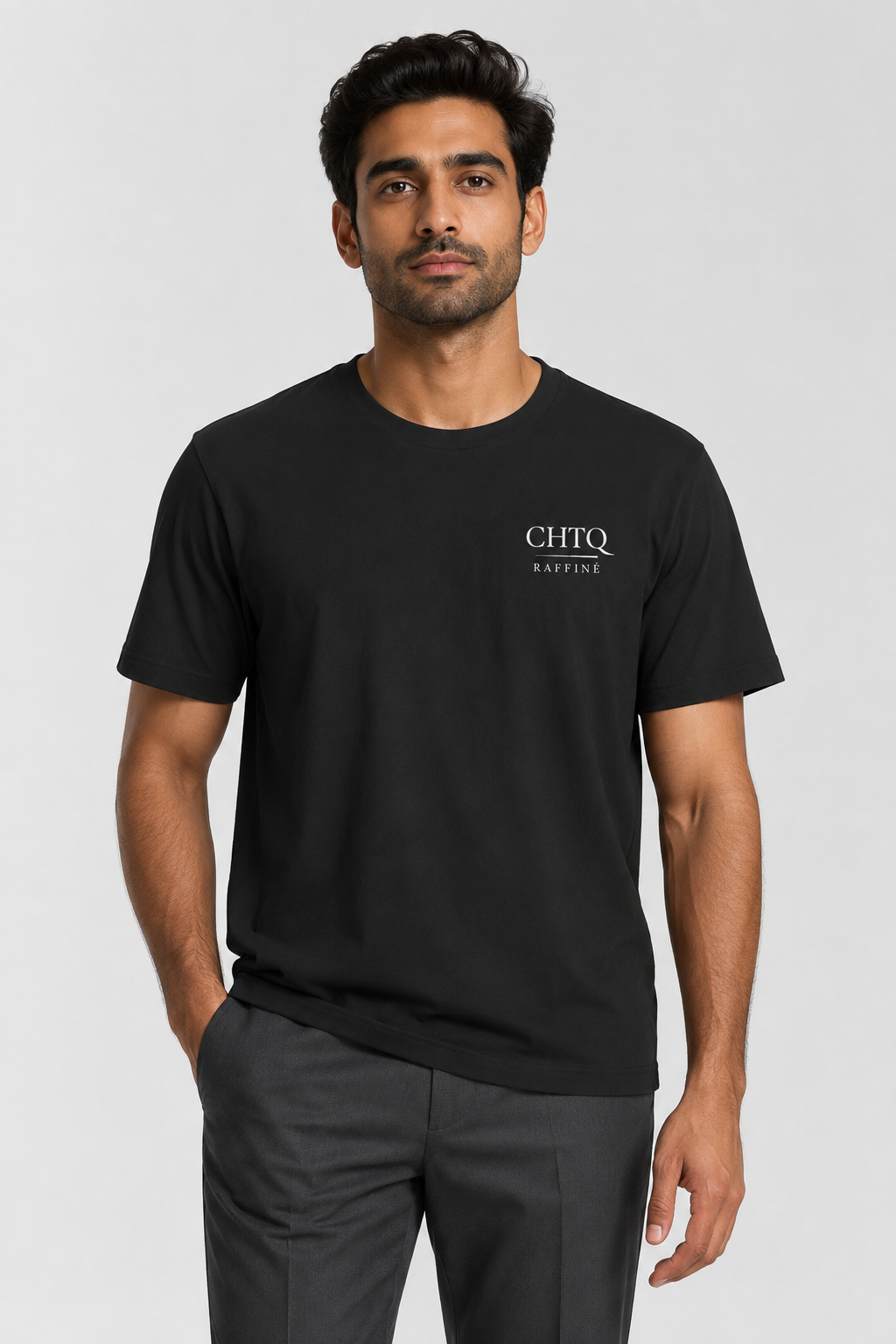 A man wearing a black short-sleeve crewneck t-shirt with 'CHTQ Raffine' printed in white on the left chest, paired with dark gray trousers, against a light gray studio background.