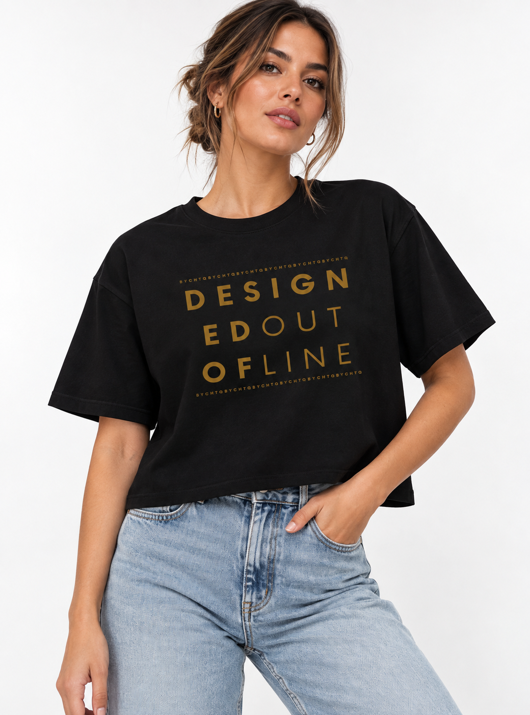 A woman wearing a black cropped boxy T-shirt with a gold typography graphic reading “DESIGNED OUT OF LINE,” paired with light-wash blue jeans against a clean white studio background.
