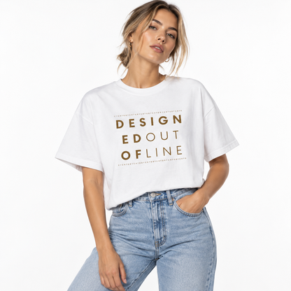 A woman wearing a white DESIGNED OUT OF LINE boxy graphic T-shirt with a gold typography print, paired with high-waisted light blue jeans against a clean white studio background.