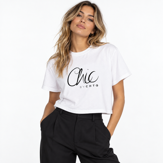 A woman wearing a white cropped boxy T-shirt with a black graphic print reading “Chic BY CHTQ” on the front, paired with black trousers, posing against a clean white studio background.