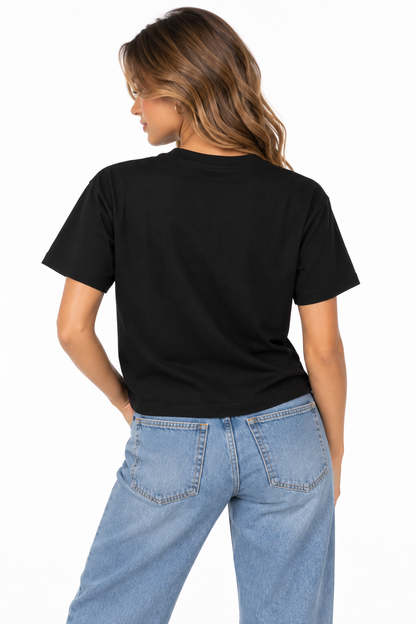 A woman shown from the back wearing a black boxy T-shirt with BEAUTIFULLY CHTQ design, paired with light blue high-waisted jeans against a clean white studio background.