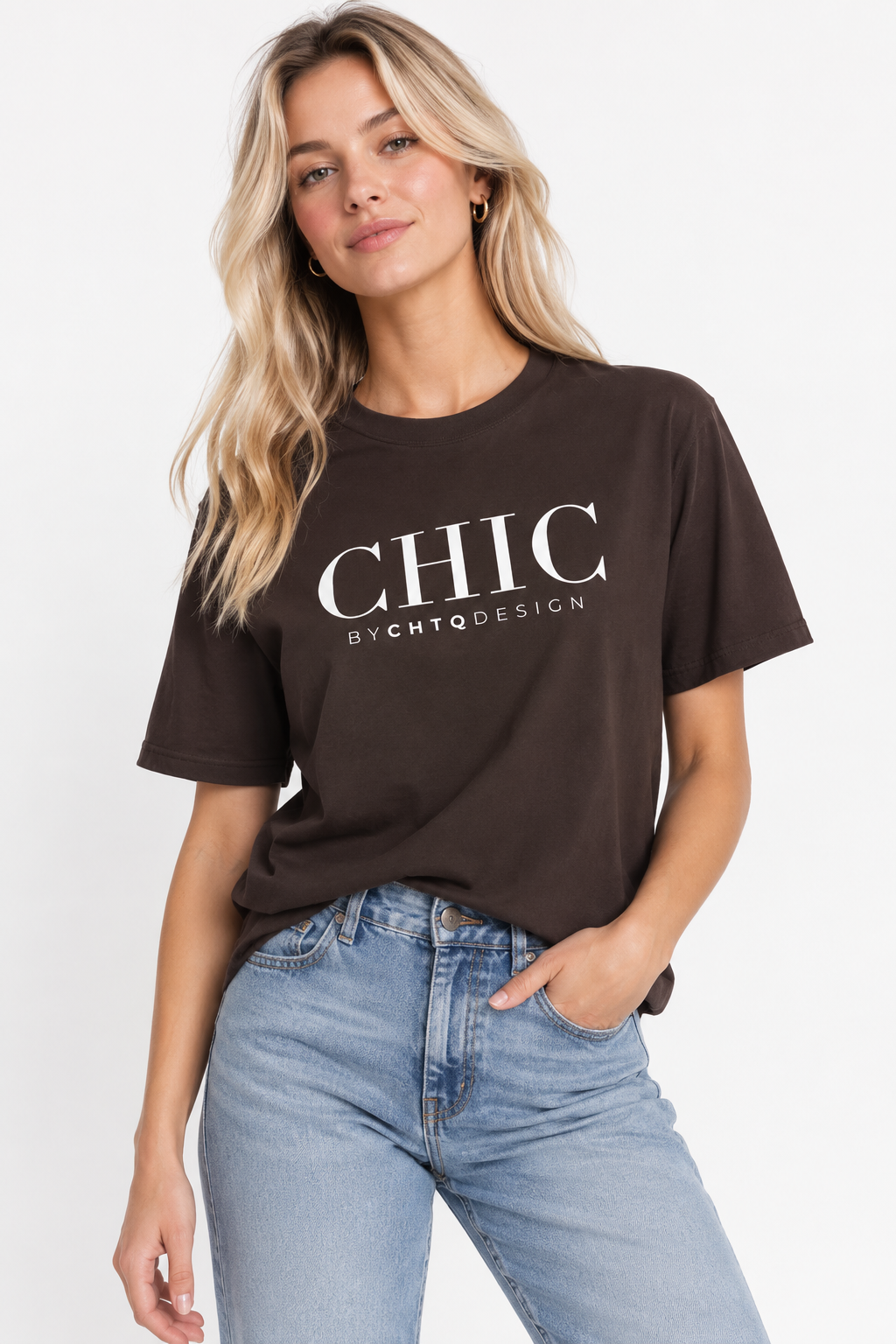 A woman wearing a brown CHIC by CHTQ Design graphic T-shirt with white typography, paired with light blue jeans against a clean white studio background.