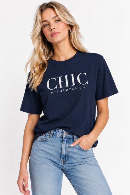 A woman wearing a nvay CHIC by CHTQ Design graphic T-shirt with white typography, paired with light blue jeans against a clean white studio background.