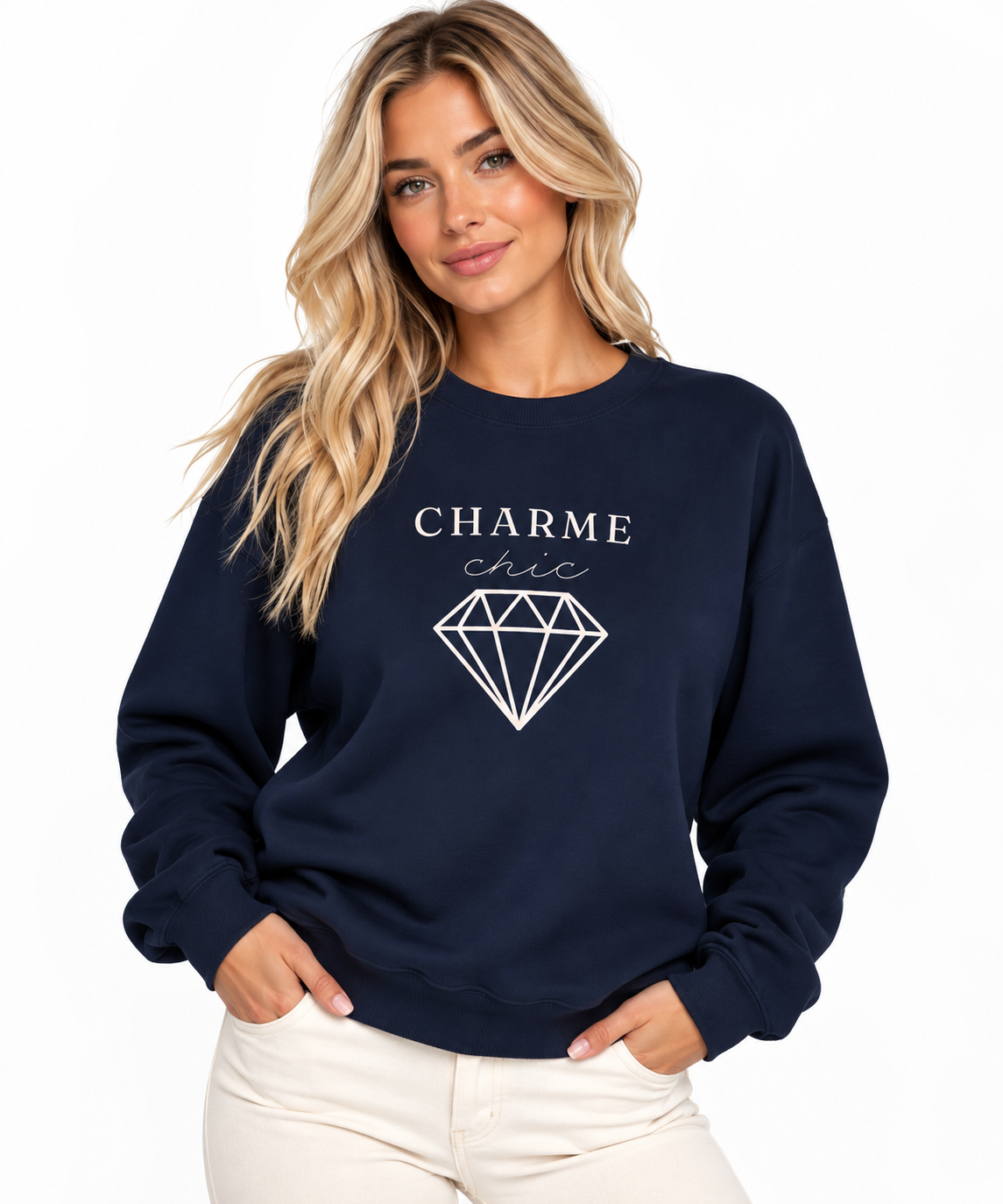 A woman modeling a navy crewneck sweatshirt featuring a light “CHARME chic” graphic with a diamond outline, paired with cream pants against a clean white studio background.