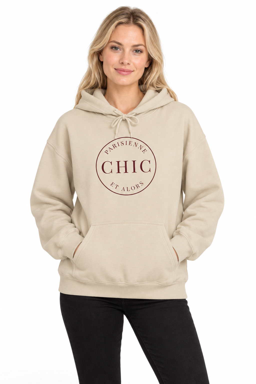 A woman wearing a beige pullover hoodie with a circular brown graphic on the chest that reads 'PARISIENNE CHIC ET ALORS', paired with black pants, against a plain white background.