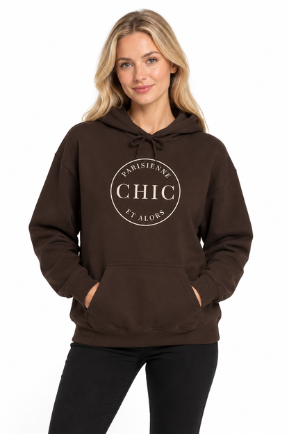 A woman modeling a dark brown pullover hoodie with a white circular graphic on the chest that reads 'PARISIANE CHIC ET ALORS'. She is wearing black pants against a plain white background.