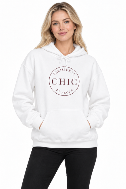 A woman wearing a white pullover hoodie with a circular chest graphic that reads 'PARISIENNE CHIC ET ALORS', paired with black pants, against a plain white background.