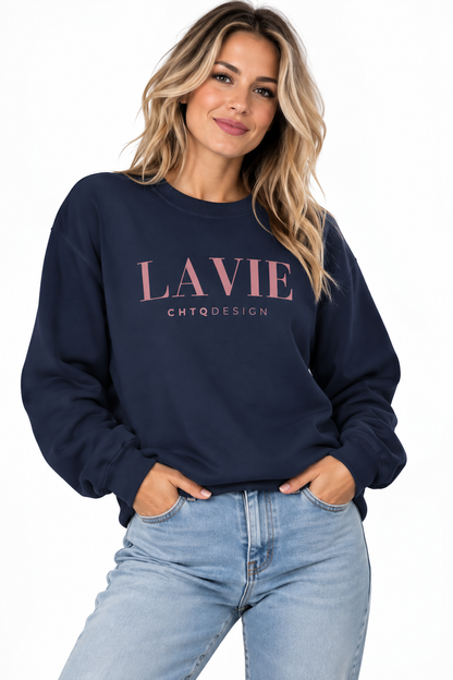 A woman wearing a navy blue crewneck sweatshirt with 'LAVIE' and 'CHTQDESIGN' printed in pink on the front, paired with light blue jeans, against a plain white background.