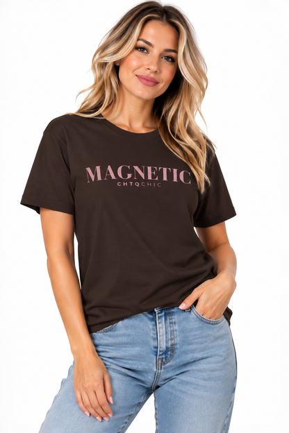 A woman wearing a brown short-sleeve graphic T-shirt with 'MAGNETIC' and smaller 'CHTQ CHIC' text printed in pink across the chest, paired with light blue jeans, against a plain white background.