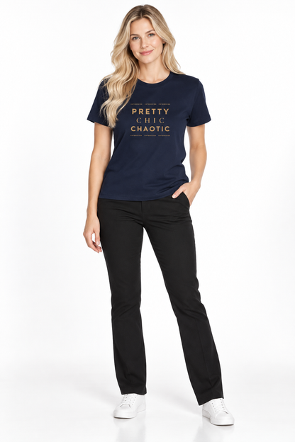 A woman modeling a navy blue graphic t-shirt with gold text that reads 'PRETTY CHIC CHAOTIC' and black pants, standing against a plain white studio background.