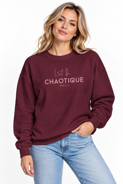A woman wearing the maroon L’ART DU CHAOTIQUE crewneck sweatshirt with minimalist front typography, paired with light blue jeans against a clean white studio background.