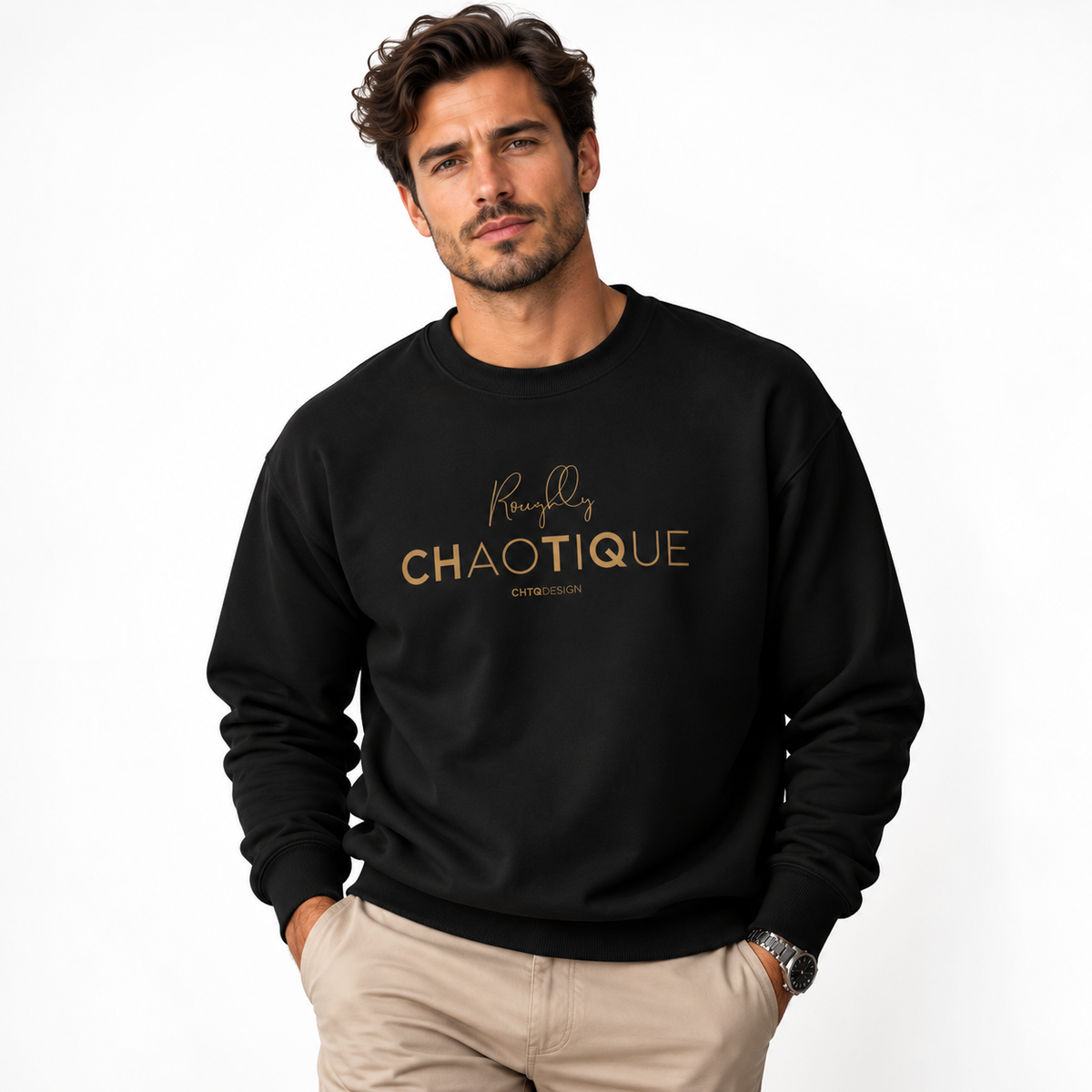 A man wearing a black Roughly Chaotique crewneck sweatshirt with gold typography on the chest, paired with beige trousers against a bright, minimalist studio background.