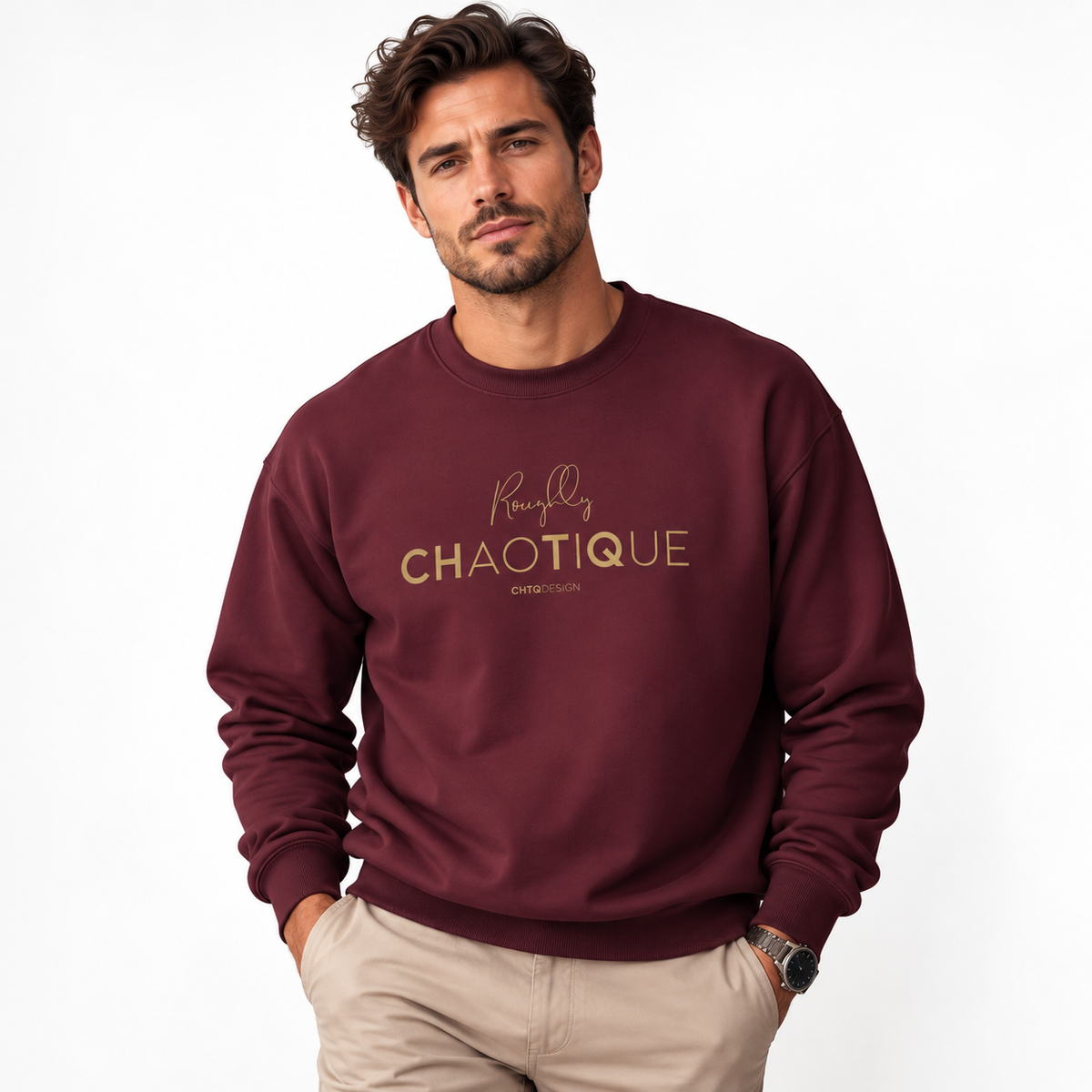A man wearing a maroon Roughly Chaotique crewneck sweatshirt with gold typography on the chest, paired with beige trousers against a bright, minimalist studio background.