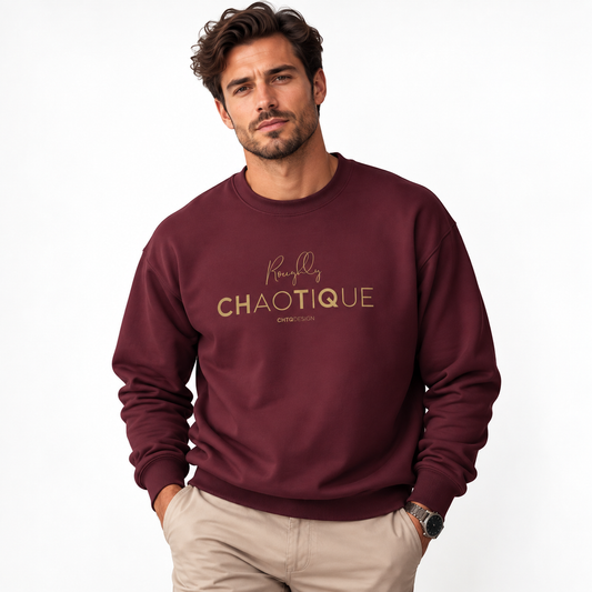 A man wearing a maroon Roughly Chaotique crewneck sweatshirt with gold typography on the chest, paired with beige trousers against a bright, minimalist studio background.