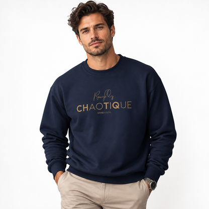 A man wearing a navy Roughly Chaotique crewneck sweatshirt with gold typography on the chest, paired with beige trousers against a bright, minimalist studio background.