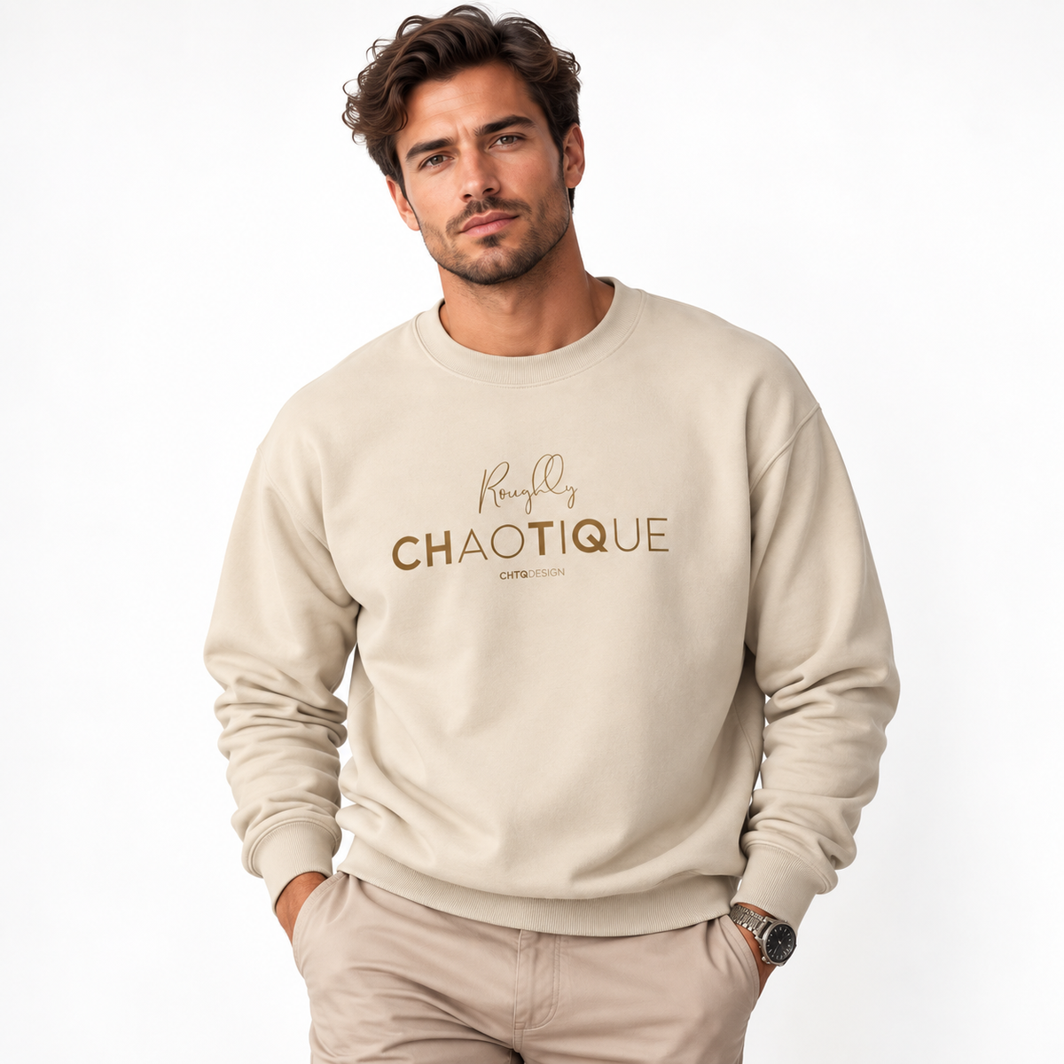 A man wearing a beige Roughly Chaotique crewneck sweatshirt with gold typography on the chest, paired with beige trousers against a bright, minimalist studio background.