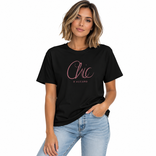 A woman wearing a black crewneck T-shirt with a rose-gold script graphic reading 'Chic D’Accord' on the chest, paired with light blue jeans against a plain white background.