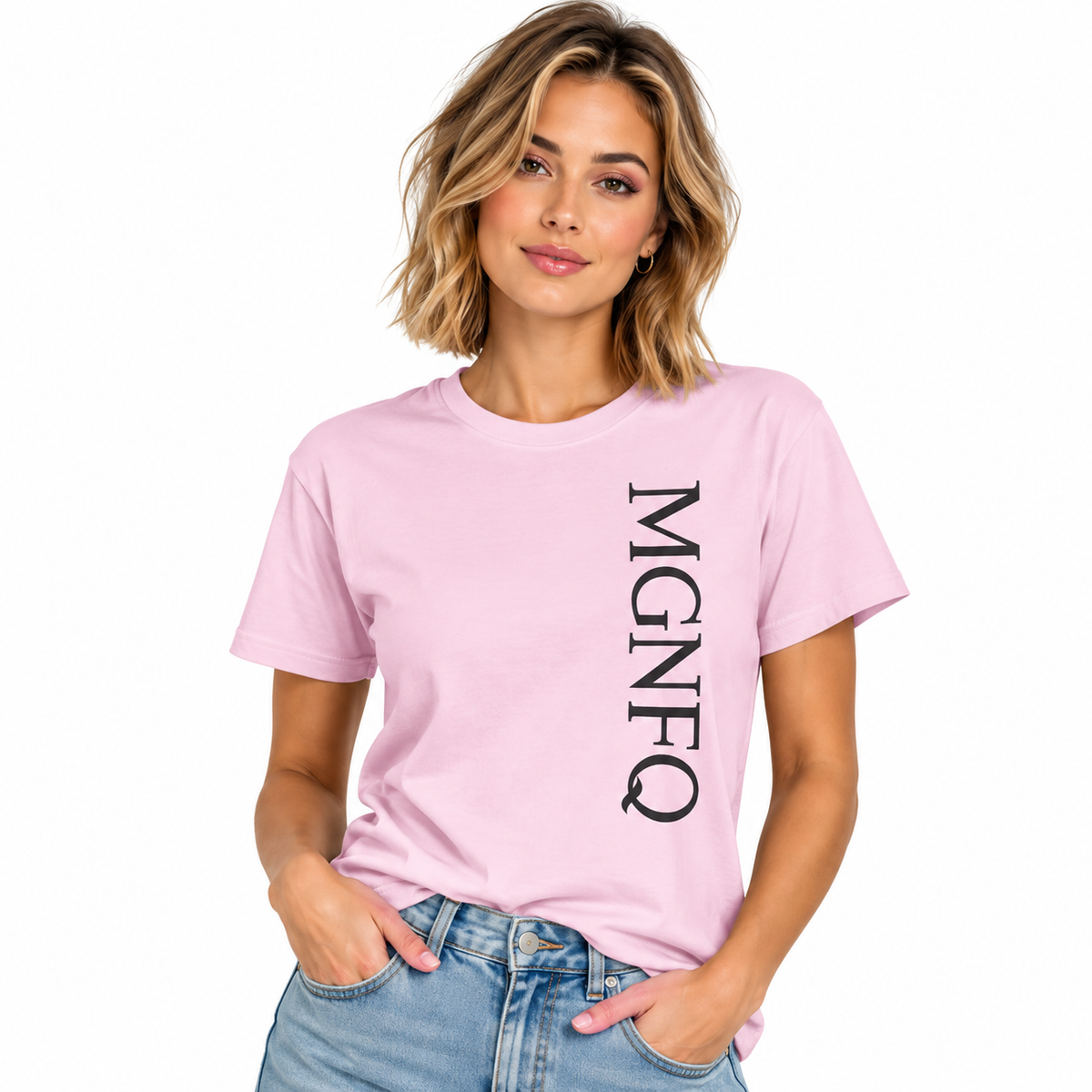 A woman wearing a light pink short-sleeve T-shirt with “MGNFQ” printed vertically in white on the front, paired with light blue jeans against a plain white studio background.