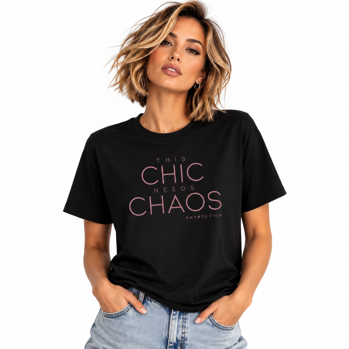 A woman wearing a black graphic t-shirt with the text 'THIS CHIC NEEDS CHAOS' in pink, paired with light-wash blue jeans, against a plain white background.