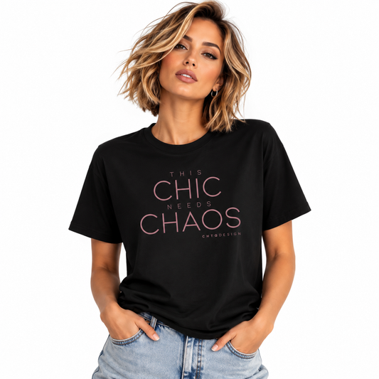 A woman wearing a black graphic t-shirt with the text 'THIS CHIC NEEDS CHAOS' in pink, paired with light-wash blue jeans, against a plain white background.