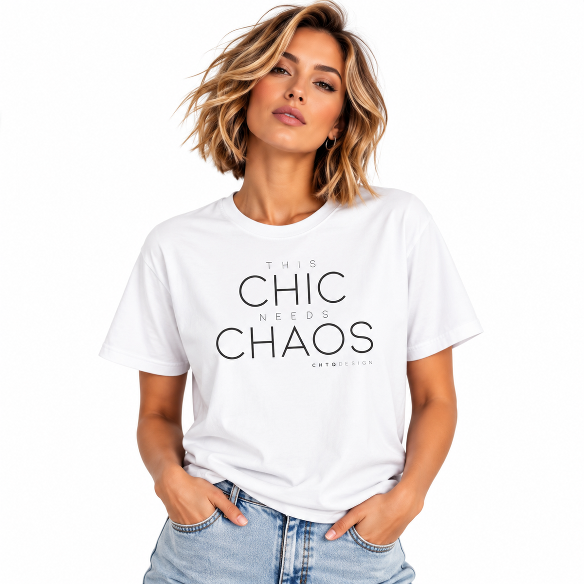 A woman with short blonde hair wearing a white graphic t-shirt with the text 'THIS CHIC NEEDS CHAOS' in black, paired with light blue jeans, against a plain white background.