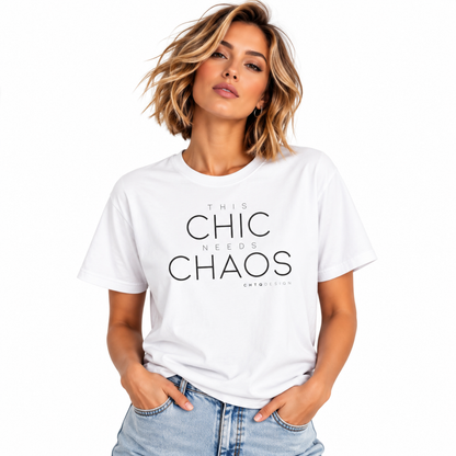A woman with short blonde hair wearing a white graphic t-shirt with the text 'THIS CHIC NEEDS CHAOS' in black, paired with light blue jeans, against a plain white background.