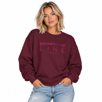 Woman wearing a maroon Designed Out of Line crewneck sweatshirt by CHTQ Design with pink graphic text.