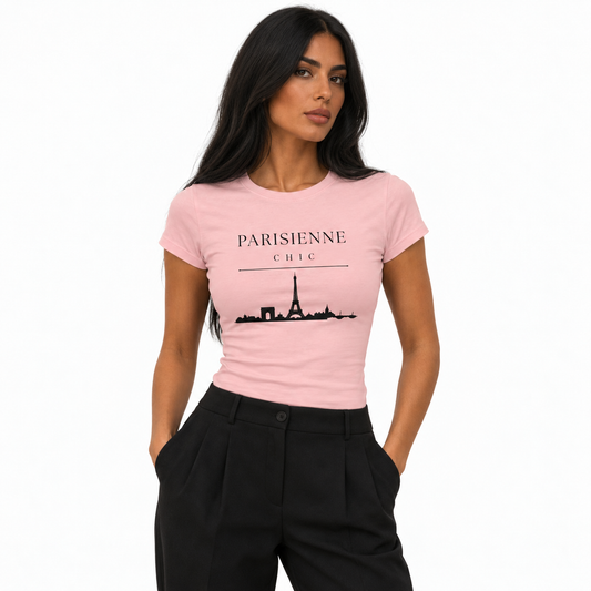 A woman modeling a light pink short-sleeve t-shirt with a black graphic of the Eiffel Tower and the text 'PARISIENNE CHIC' on the front, paired with black trousers, against a plain white background.