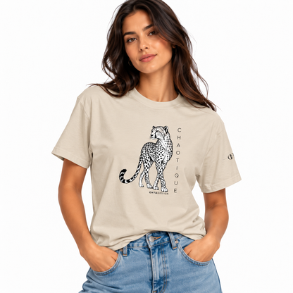 Woman wearing a sand CHAOTIQUE graphic T-shirt with hand-drawn cheetah illustration and vertical CHAOTIQUE text, styled with light blue jeans.