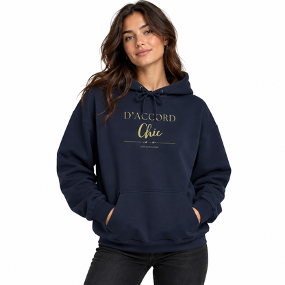 A woman wearing a navy blue pullover hoodie with 'D'ACCORD Chic' printed in gold on the chest, paired with black jeans, against a plain white background.