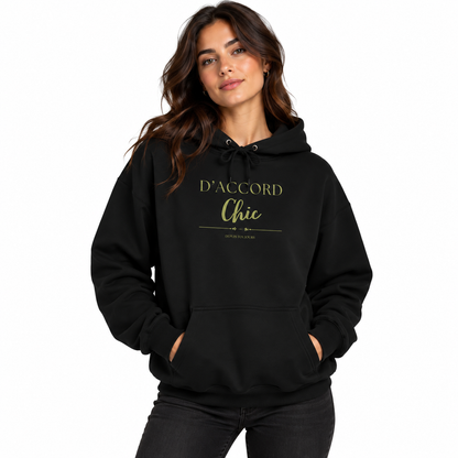 A woman modeling a black pullover hoodie with 'D'ACCORD Chic' printed in gold on the chest, set against a plain white background.