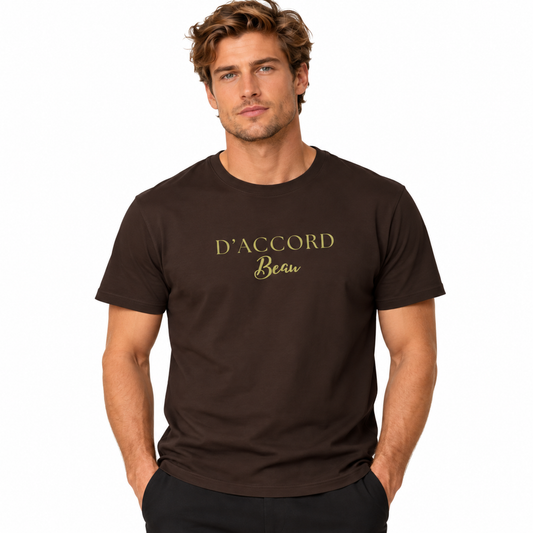 A man wearing a dark brown crewneck t-shirt with 'D'ACCORD Beau' printed in gold lettering on the chest, set against a plain white background.