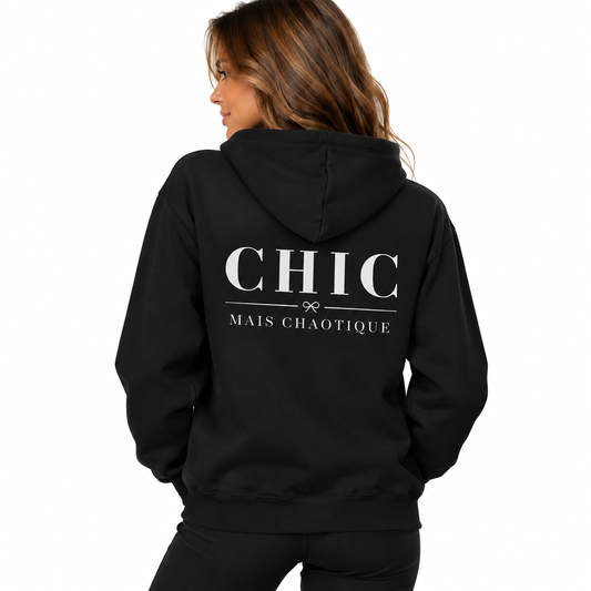 A woman shown from the back wearing a black hoodie with 'CHIC MAIS CHAOTIQUE' printed in white text on the back, against a plain white background.
