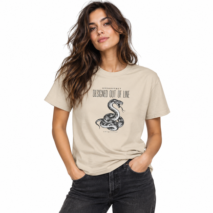 Female model wearing a cream beige UNSNAKEBLY snake graphic T-shirt with dark jeans against a white studio background.