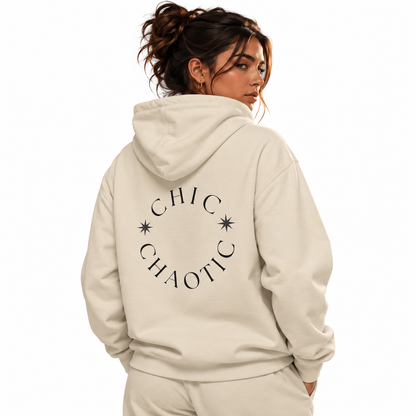 A woman shown from the back wearing a cream-colored hoodie with a black circular graphic that reads 'CHIC CHAOTIC' and small star accents. The background is solid white.