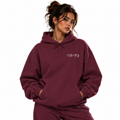 A woman wearing a matching burgundy sweatshirt and pants set, featuring the text 'CH-TQ' printed in white on the left chest, set against a plain white background.