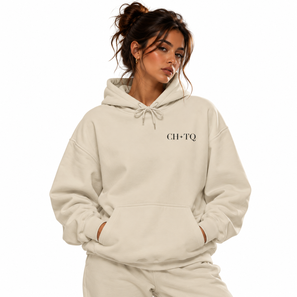 A woman wearing a light cream-colored hoodie with 'CH-TQ' printed in black serif font on the left chest, paired with matching sweatpants, set against a solid white background.