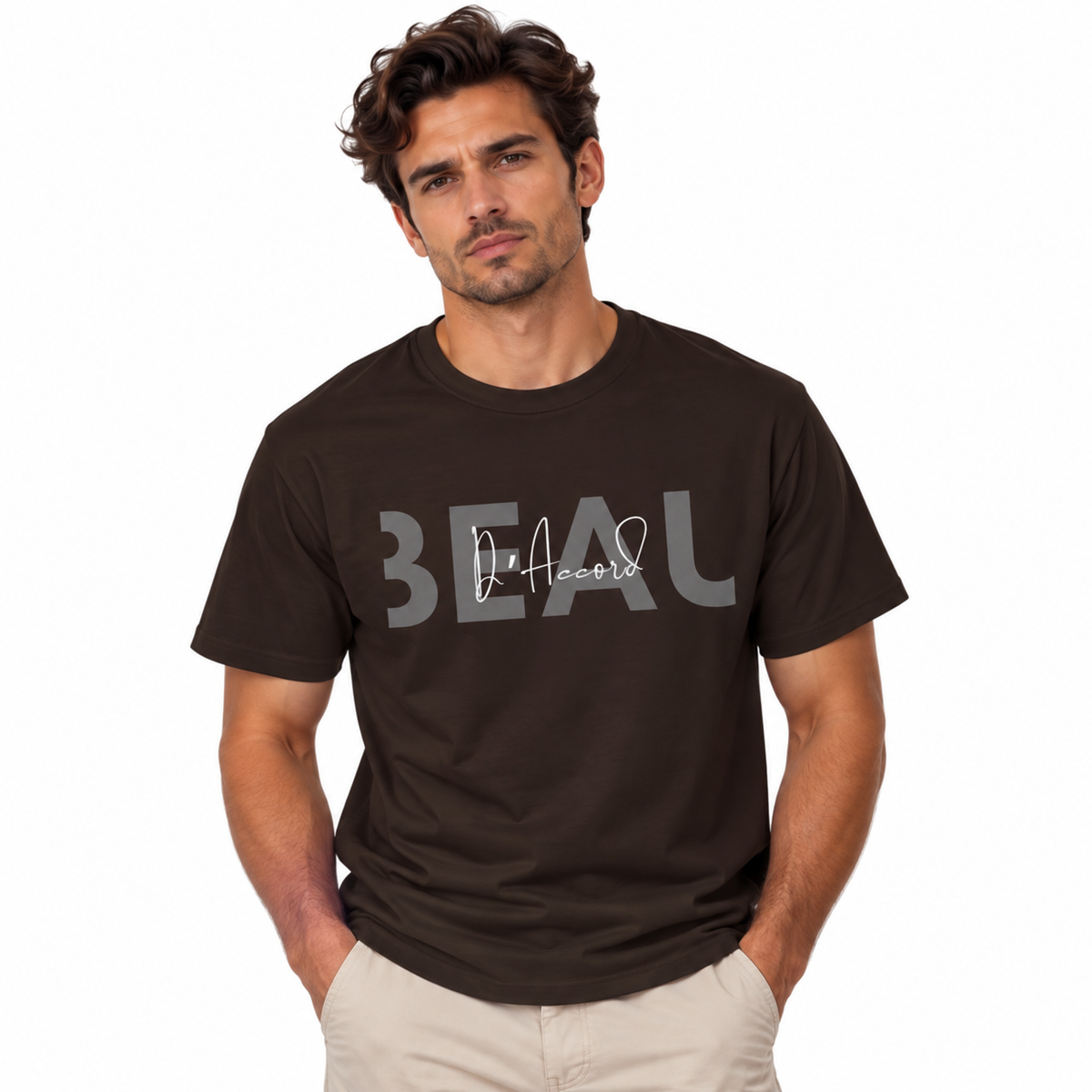 A man wearing a dark brown Dark chocolate brown BEAU D’Accord graphic T-shirt featuring large grey BEAU lettering with white handwritten D’Accord script across the chest, paired with light beige pants, against a plain white background.