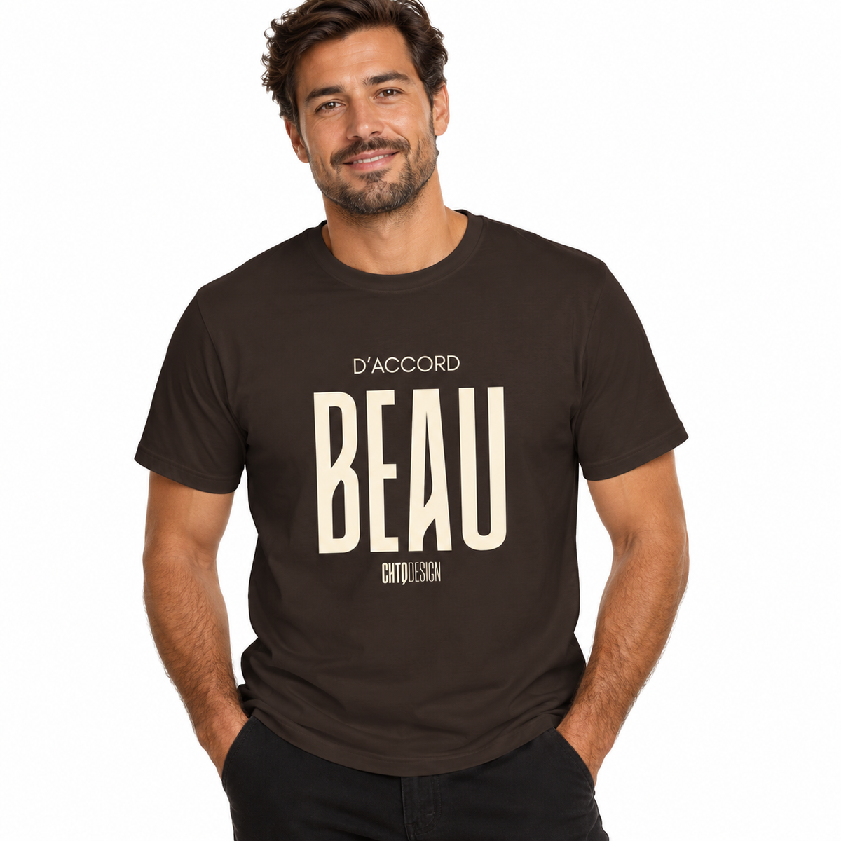 Male model wearing a dark chocolate brown D’ACCORD BEAU Graphic T-Shirt by CHTQ Design with cream lettering and black trousers on a white studio background.
