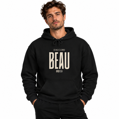 A man wearing a black pullover hoodie with a beige graphic print on the front that reads 'D'ACCORD BEAU' against a plain white background.