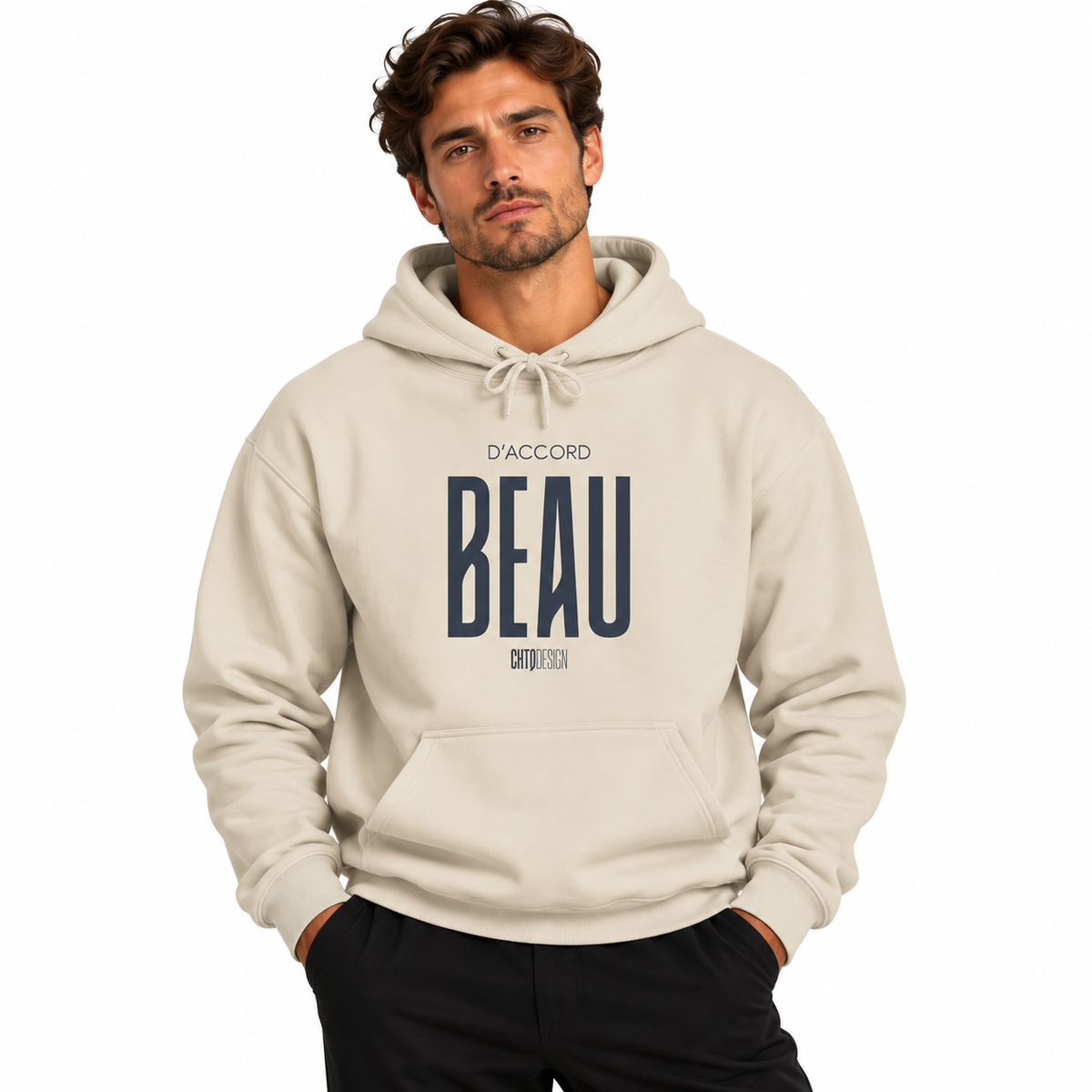 A man wearing a beige pullover hoodie with a navy blue graphic print on the front that reads 'D'ACCORD BEAU', paired with black pants, against a plain white background.