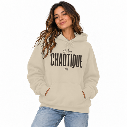 Woman modeling a sand beige Je Suis CHAOTIQUE CHIC hoodie with dark chest lettering, paired with light blue jeans.