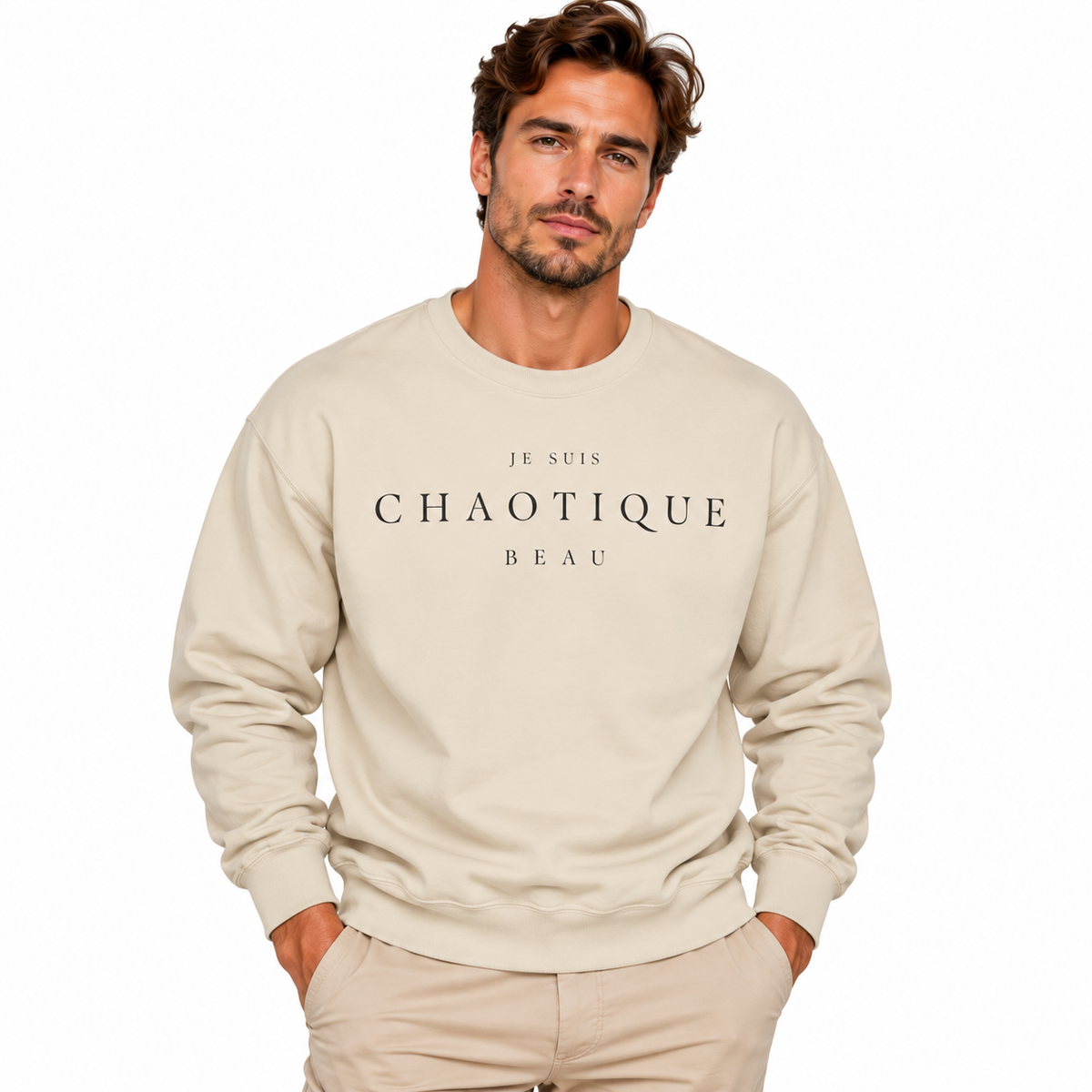 A man wearing a beige crewneck sweatshirt with the text 'JE SUIS CHAOTIQUE BEAU' printed in white across the chest, paired with beige pants, set against a plain white background.